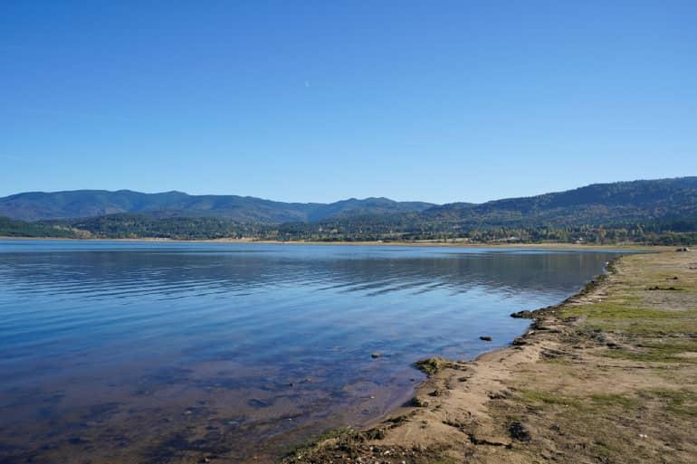Un tranquilo lago en la ciudad de Velingrado, en Bulgaria, rodeado de bosques con una pequeña orilla rocosa.
