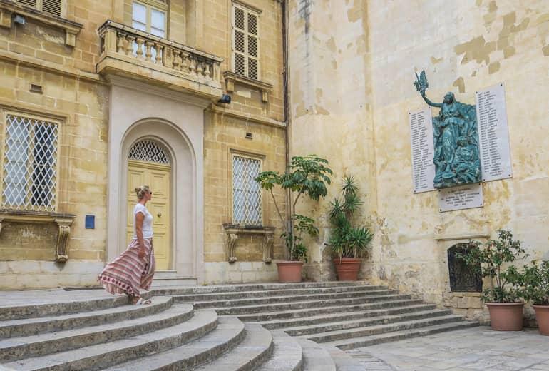 Woman looks at a monument on a house wall in Vittoriosa, one of the 'Three Cities'