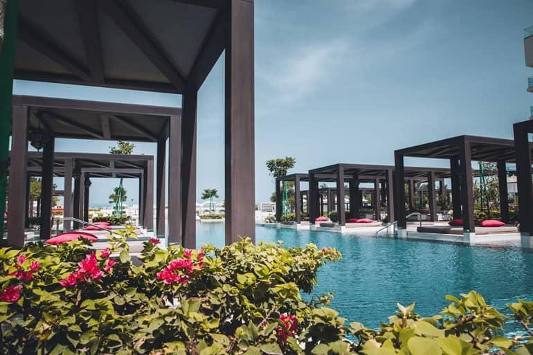 Un amplio río de piscina fluye a través del hotel W Muscat en Omán, pasando por la vegetación y las islas de reposo de madera cubiertas.