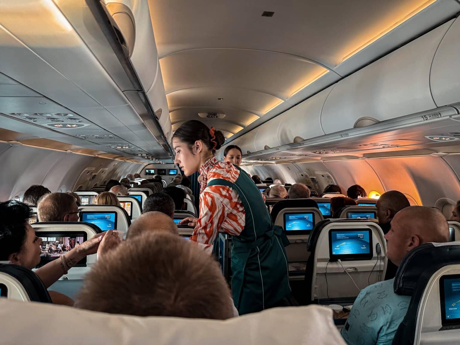 La cabina completamente ocupada de un avión de la aerolínea Uzbekistan Airways. Las azafatas circulan por el pasillo con un carrito.