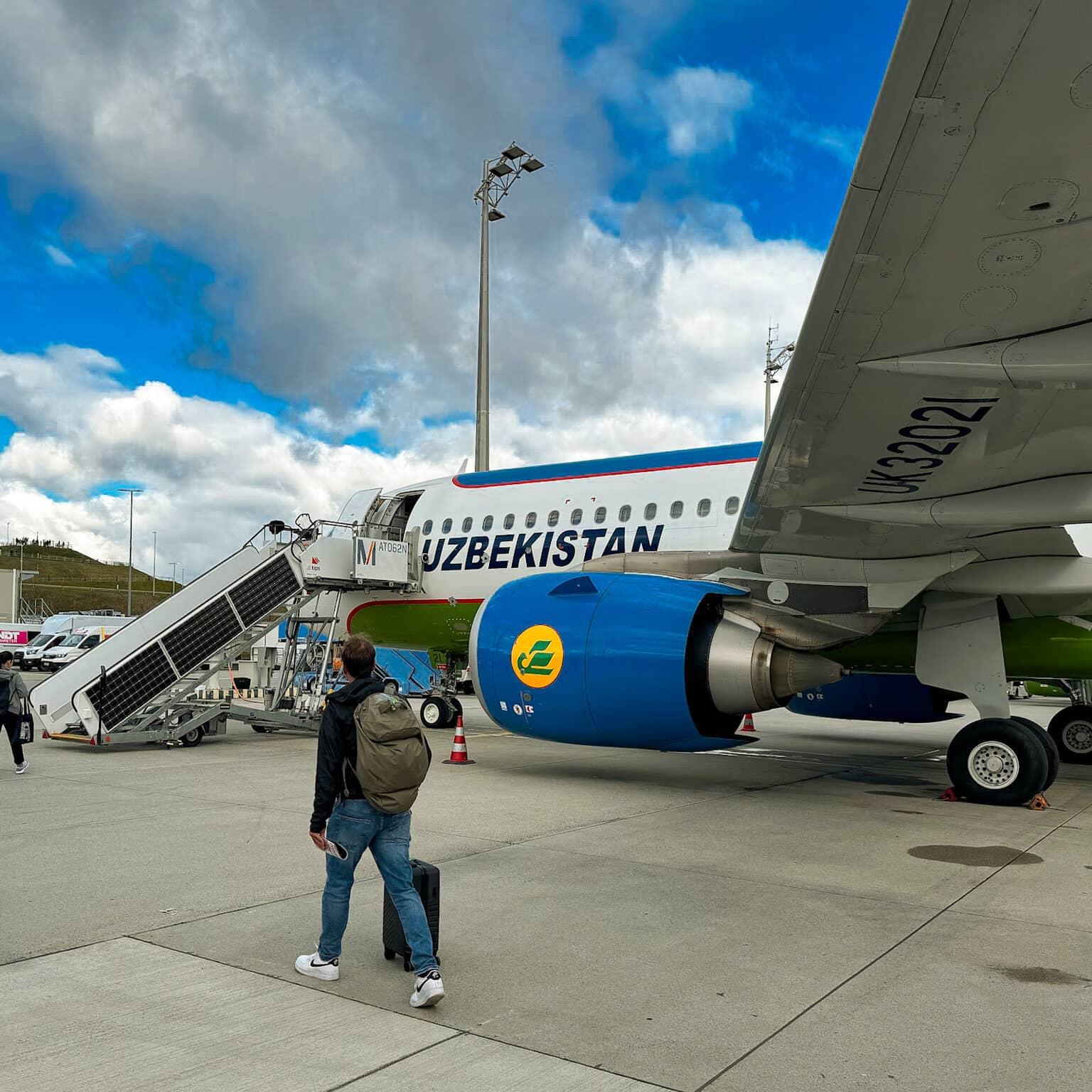 Un avión de la aerolínea Uzbekistan Airways en la pista. Varios pasajeros se dirigen a la entrada a través de una escalera.