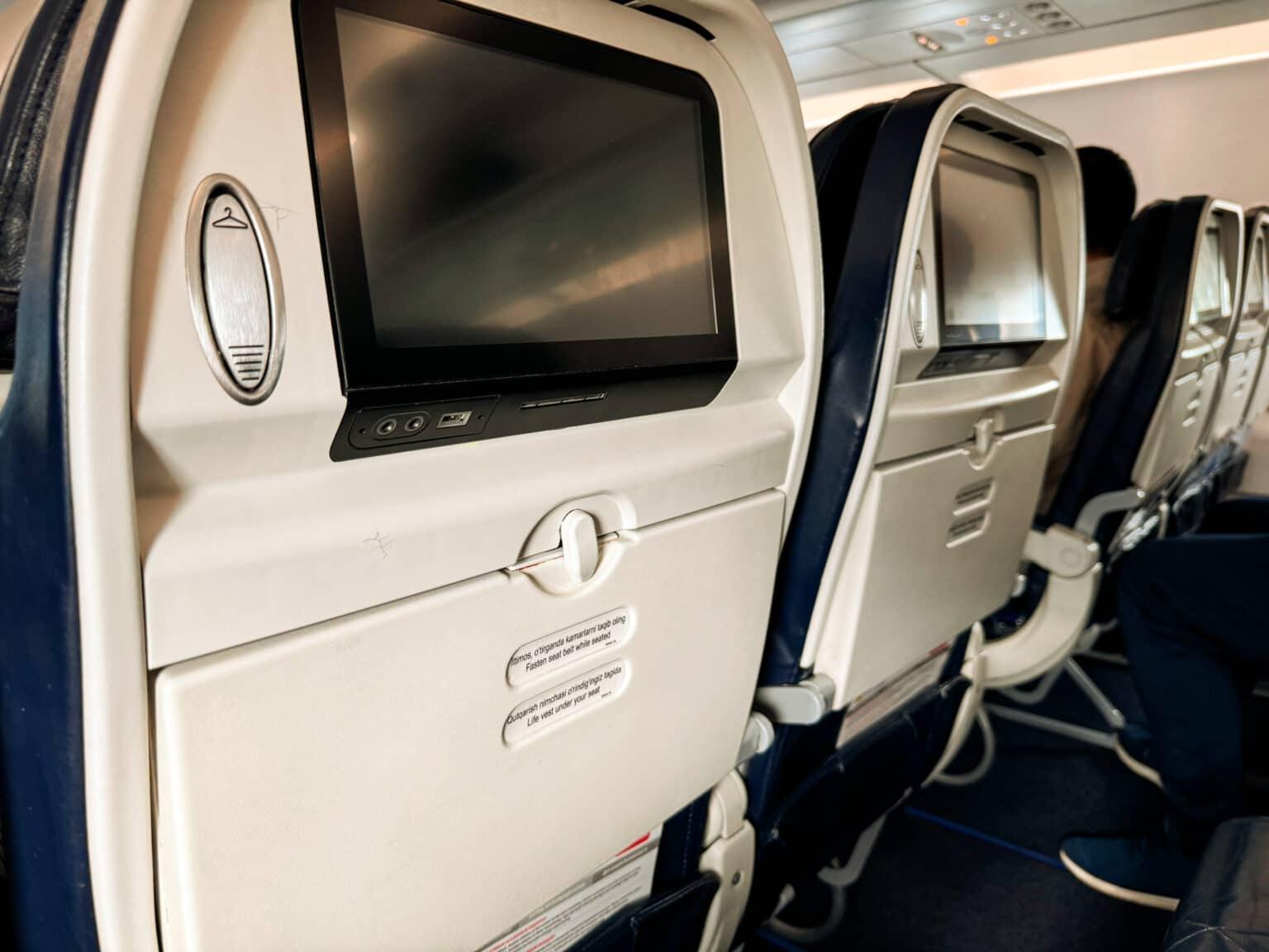 La parte posterior de una fila de asientos en un avión de la aerolínea Uzbekistan Airways con pantallas apagadas.