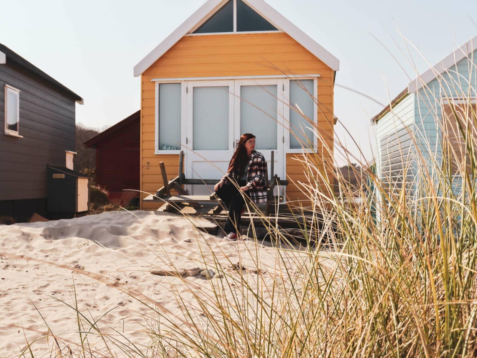 Una mujer sentada frente a una cabaña de playa amarilla en Mudeford Sands en el sur de Inglaterra.