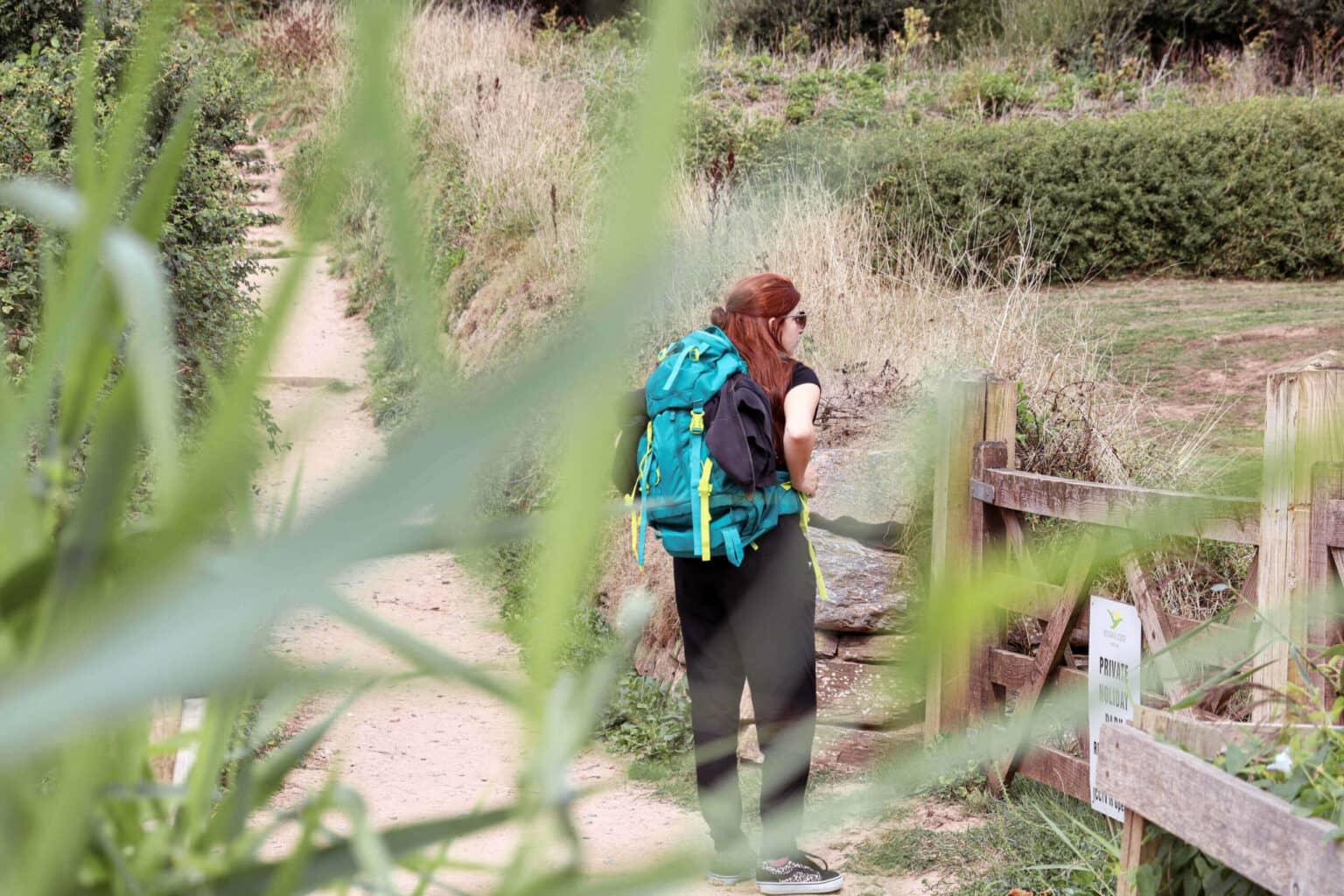 Una mujer pelirroja se encuentra detrás de una cerca de madera en el South West Coast Path en el sur de Inglaterra.