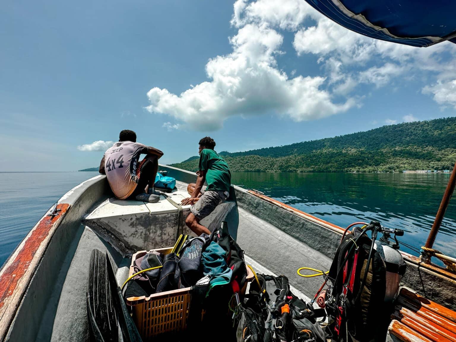 Two men sitting on the bow of a boat, behind them diving equipment.