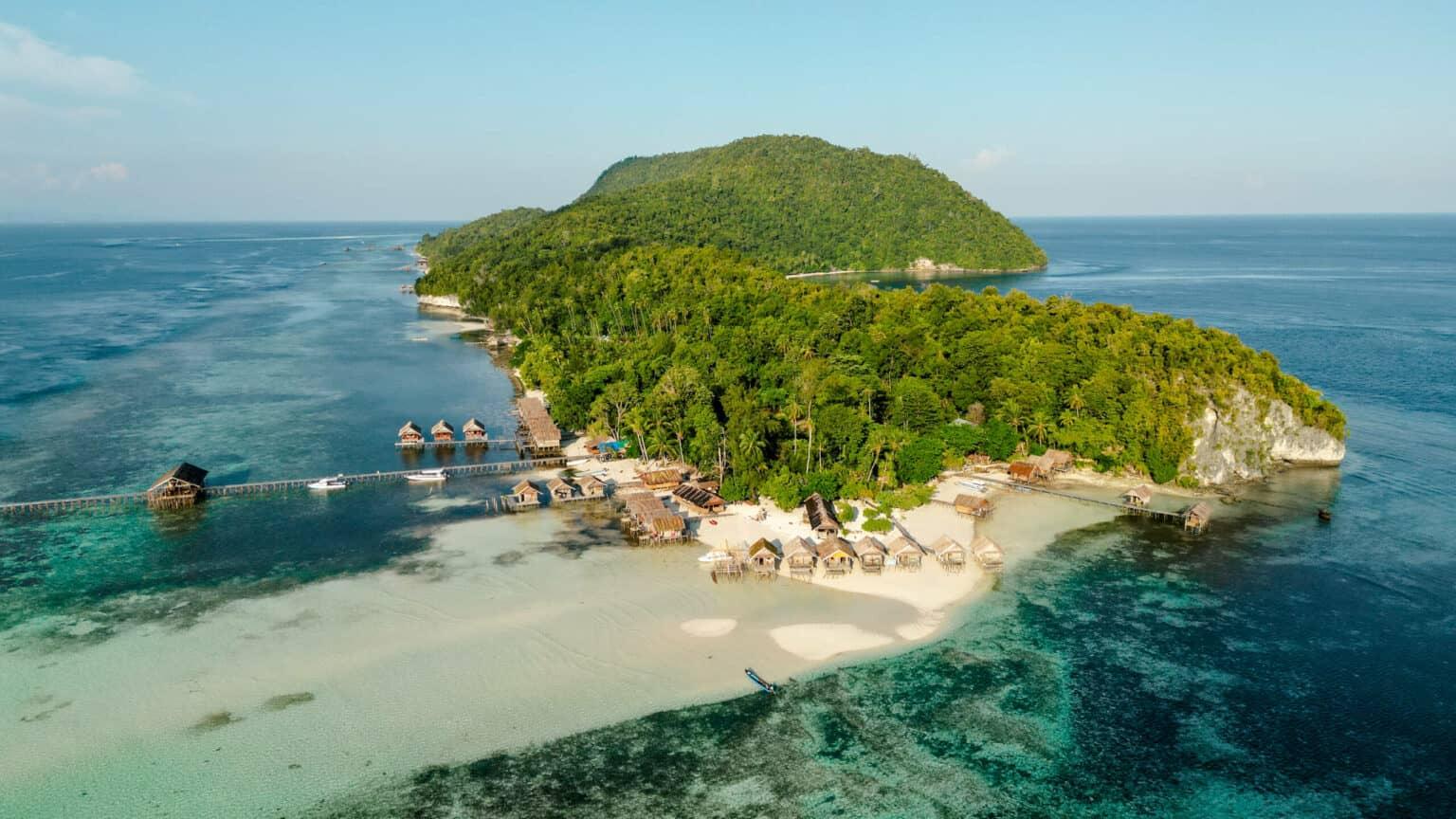 Small wooden cabins in the foreground of the green island of Raja Ampat.