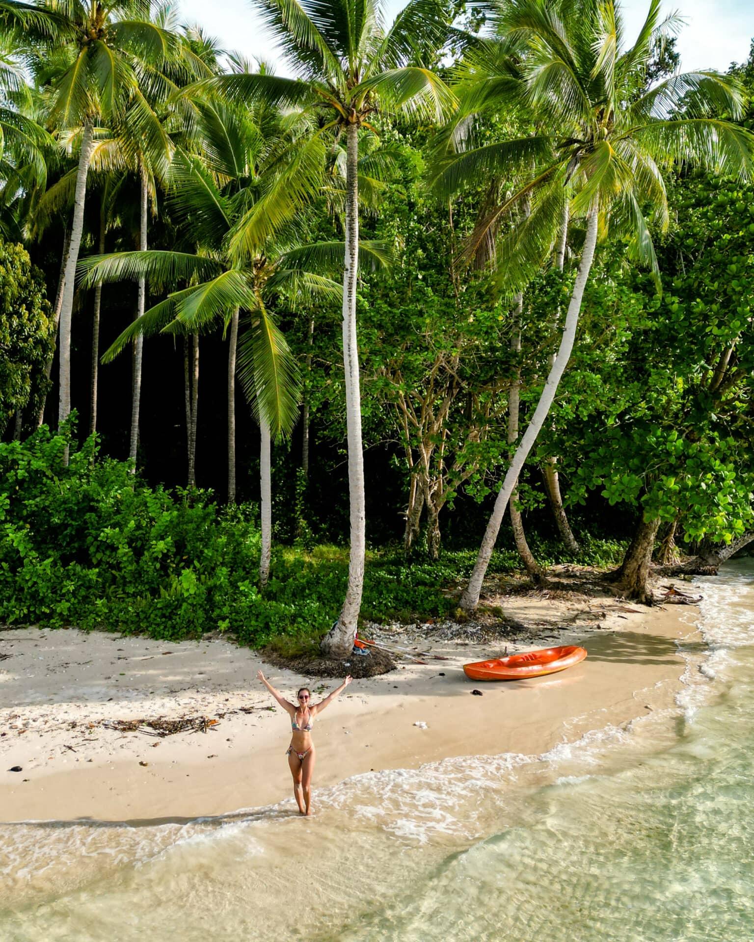 Blogger Nina stands on a deserted beach in Raja Ampat with an orange kayak.
