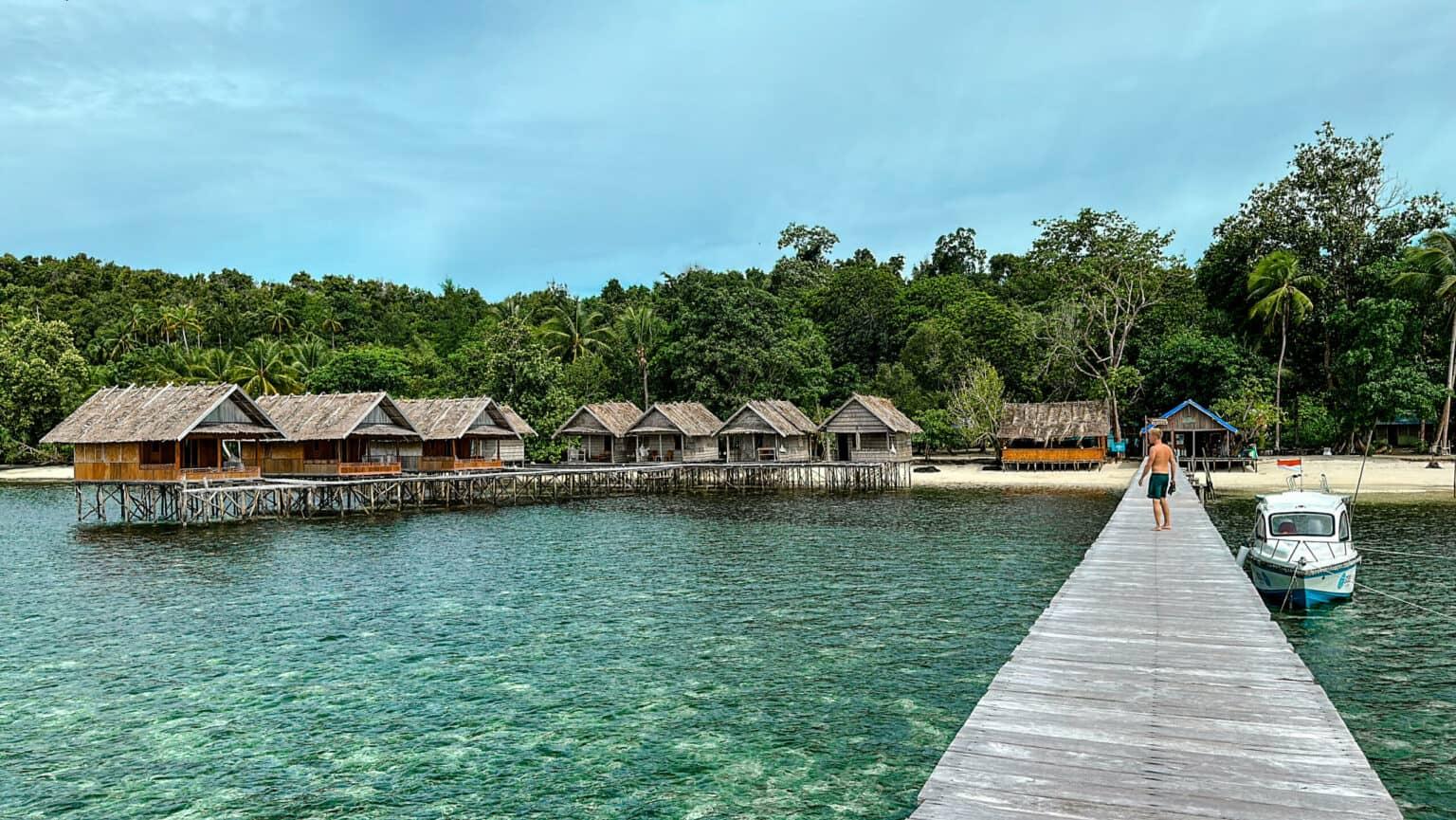 Blogger Tom stands on a wooden pier looking at the over-water bungalows of a homestay in Raja Ampat.