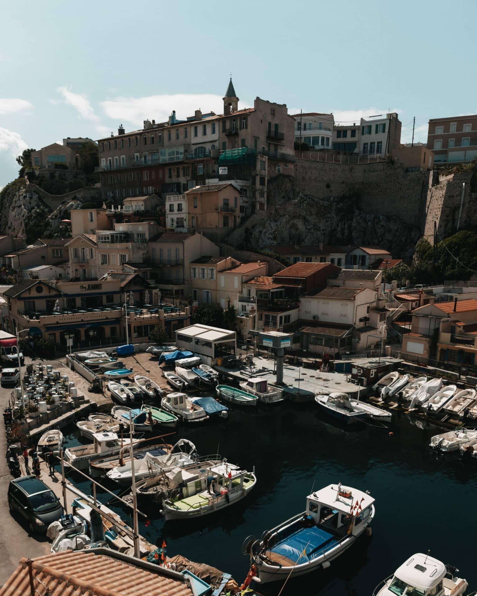 Colorful fishing boats in a small harbor in Marseille, with many colorful houses in the background.