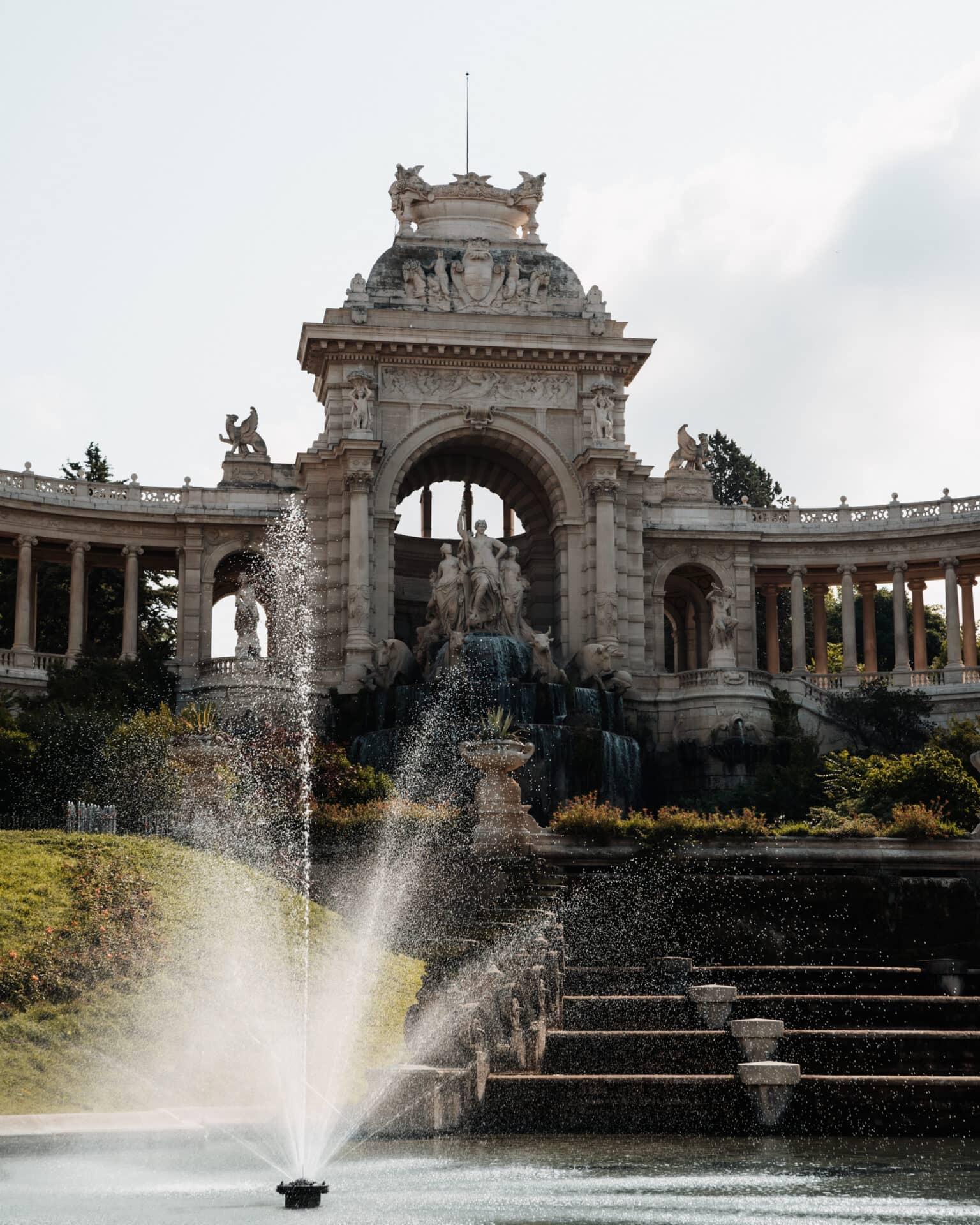 A fountain in front of the Palais Longchamp, surrounded by white statues and decorations.