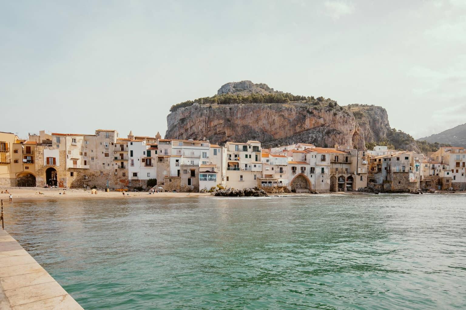 A city beach in Cefalù, with a rock towering over the city in the background.