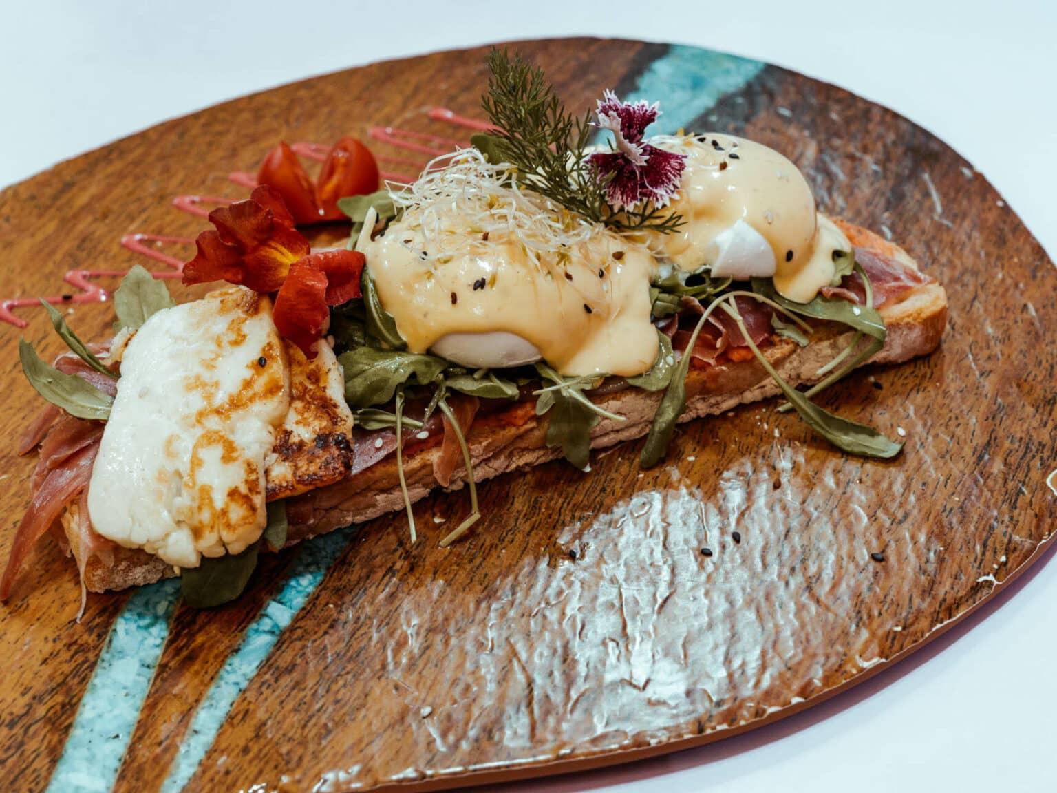 En el Crustina Eggullera, que se sirve en el Eixampeling Brunch Café & Bar en Barcelona, hay una rebanada de pan tostado con jamón serrano, huevos poché, salsa holandesa, rúcula y tomates.