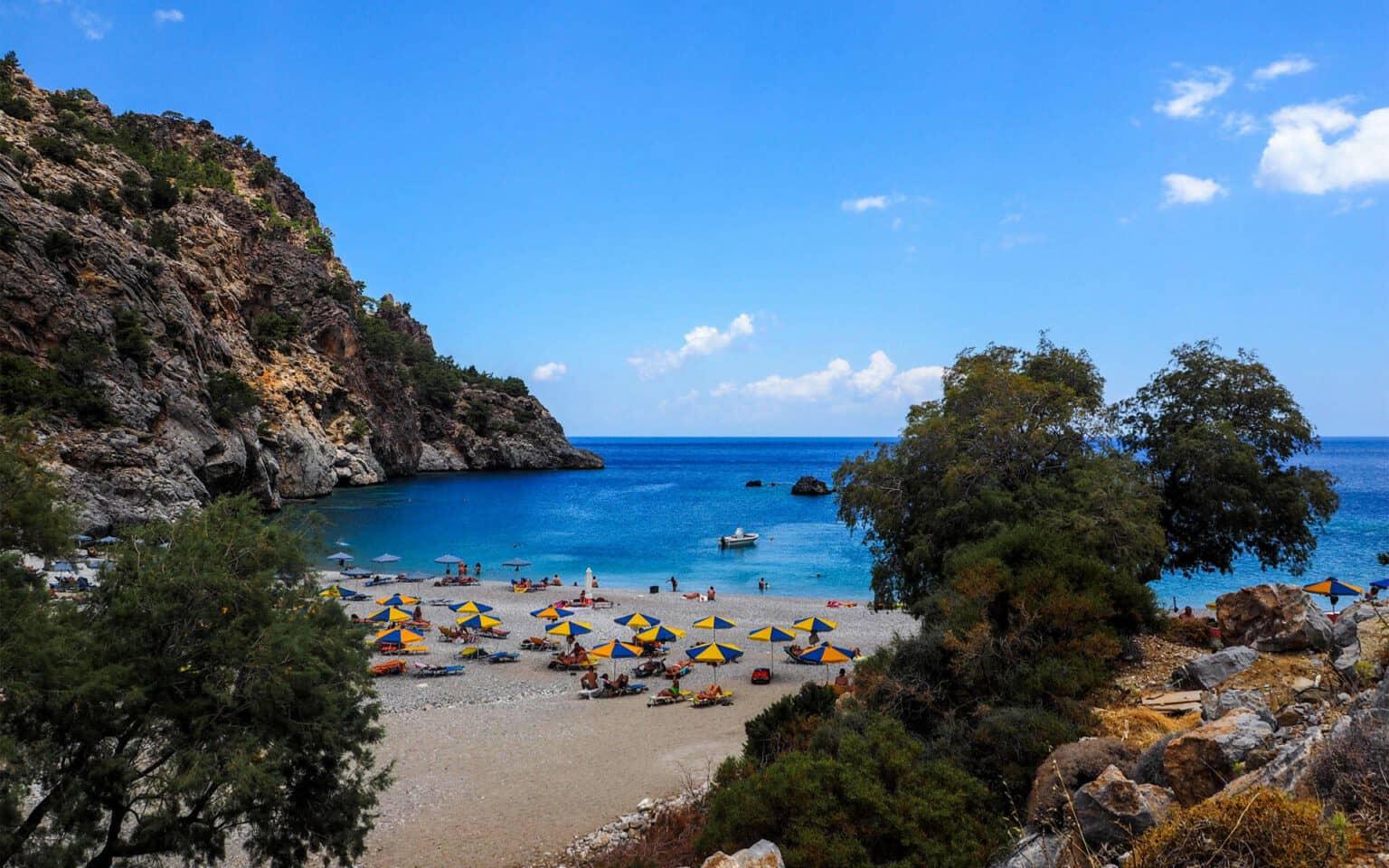 On Karpathos, between bushes and pine forests along the roadside lies Acháta Beach, where yellow and blue umbrellas protect its guests from the sun.
