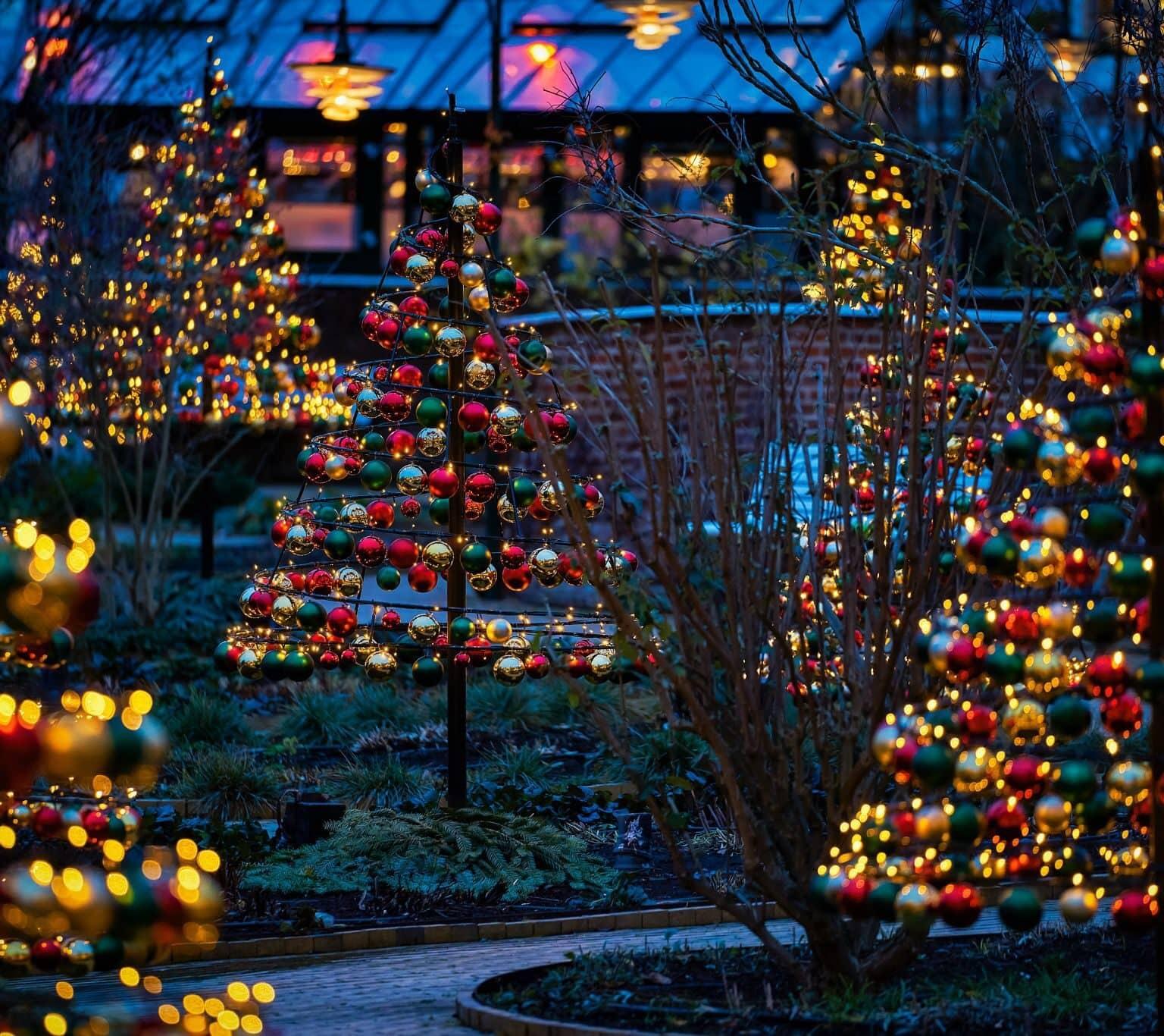 Several small Christmas trees made of ornaments and string lights lining a narrow path in Tivoli amusement park.