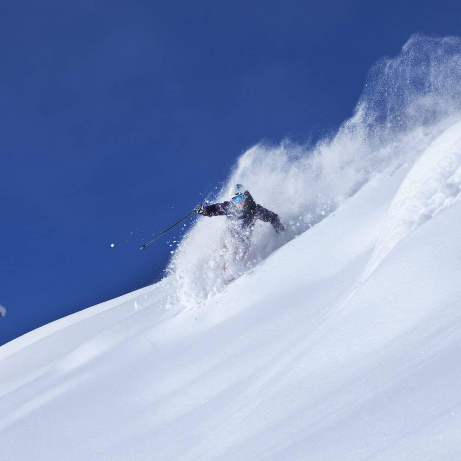 A skier makes fresh powder turns off the slope on a sunny day in Colorado.