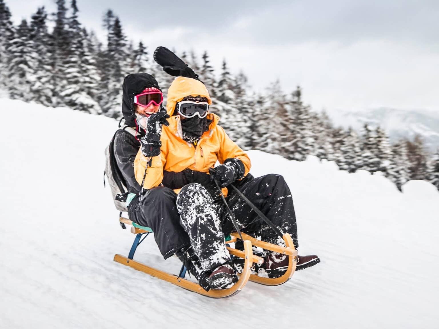 Two people enjoy a fast descent on a wooden sled in the Wildkogel ski area.