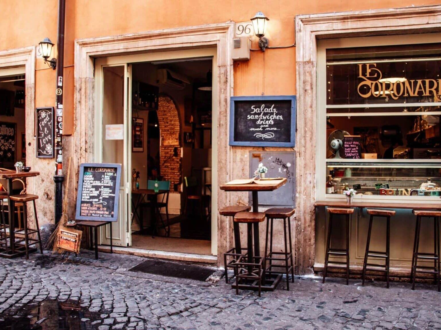 Vista del restaurante Le Coronarie en Roma con mesas altas y taburetes en primer plano.