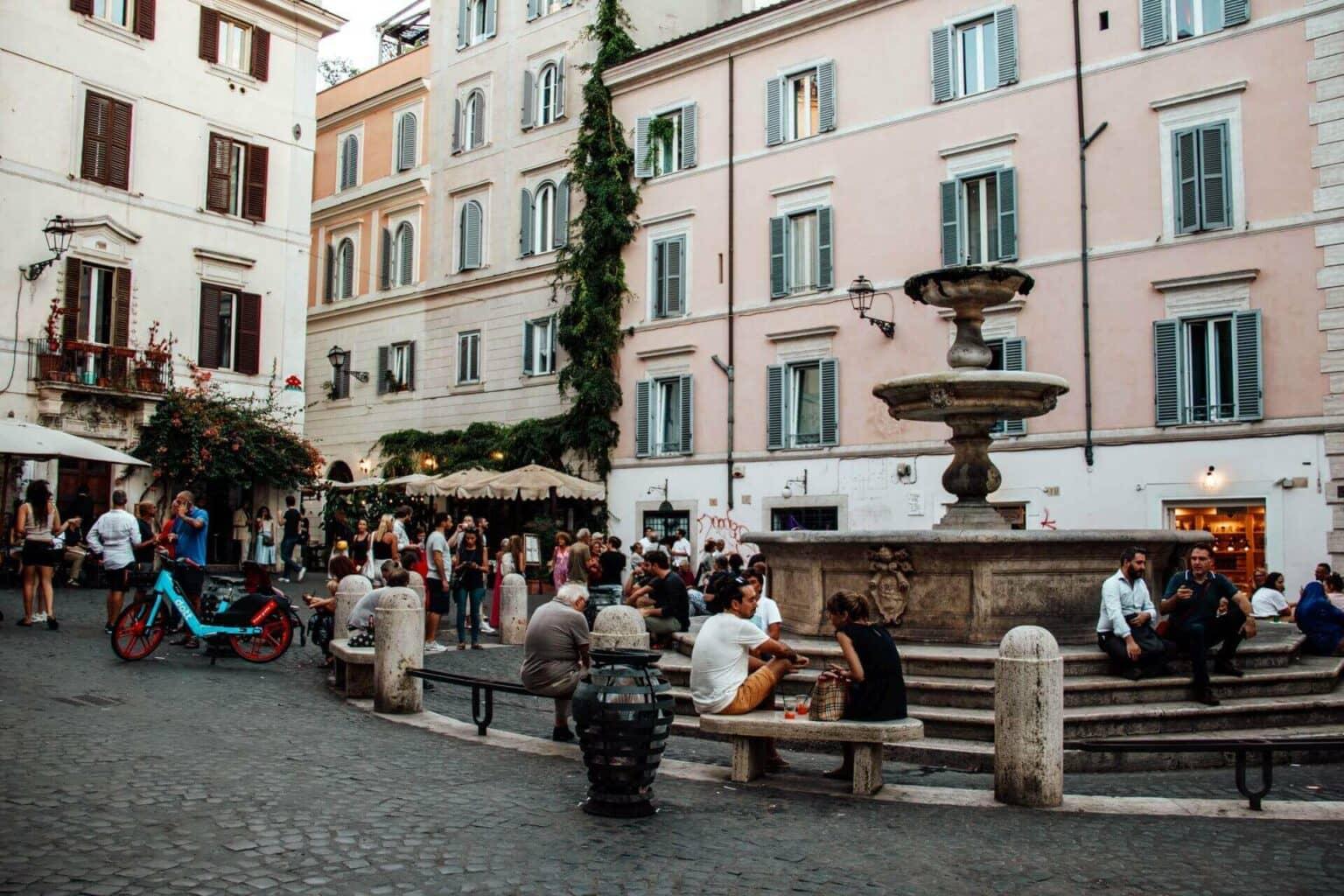 Muchas personas se sientan en los bancos de piedra y escalones en la crepuscular Piazza della Madonna dei Monti en Roma.