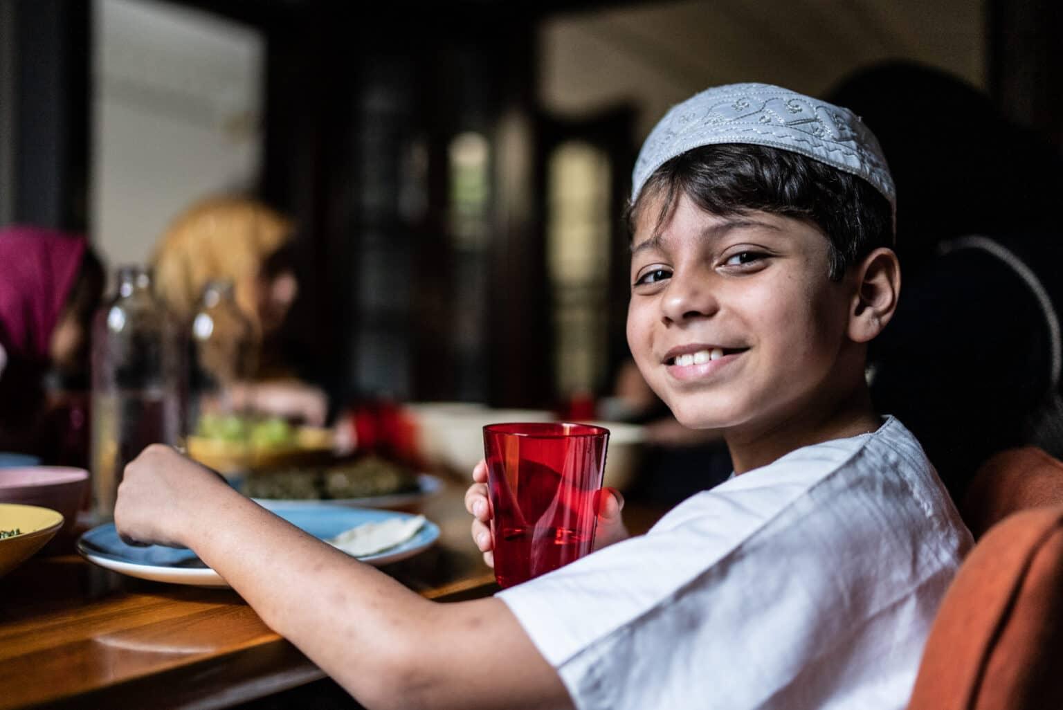 Portrait of a Muslim boy sitting at a table with his family, eating.