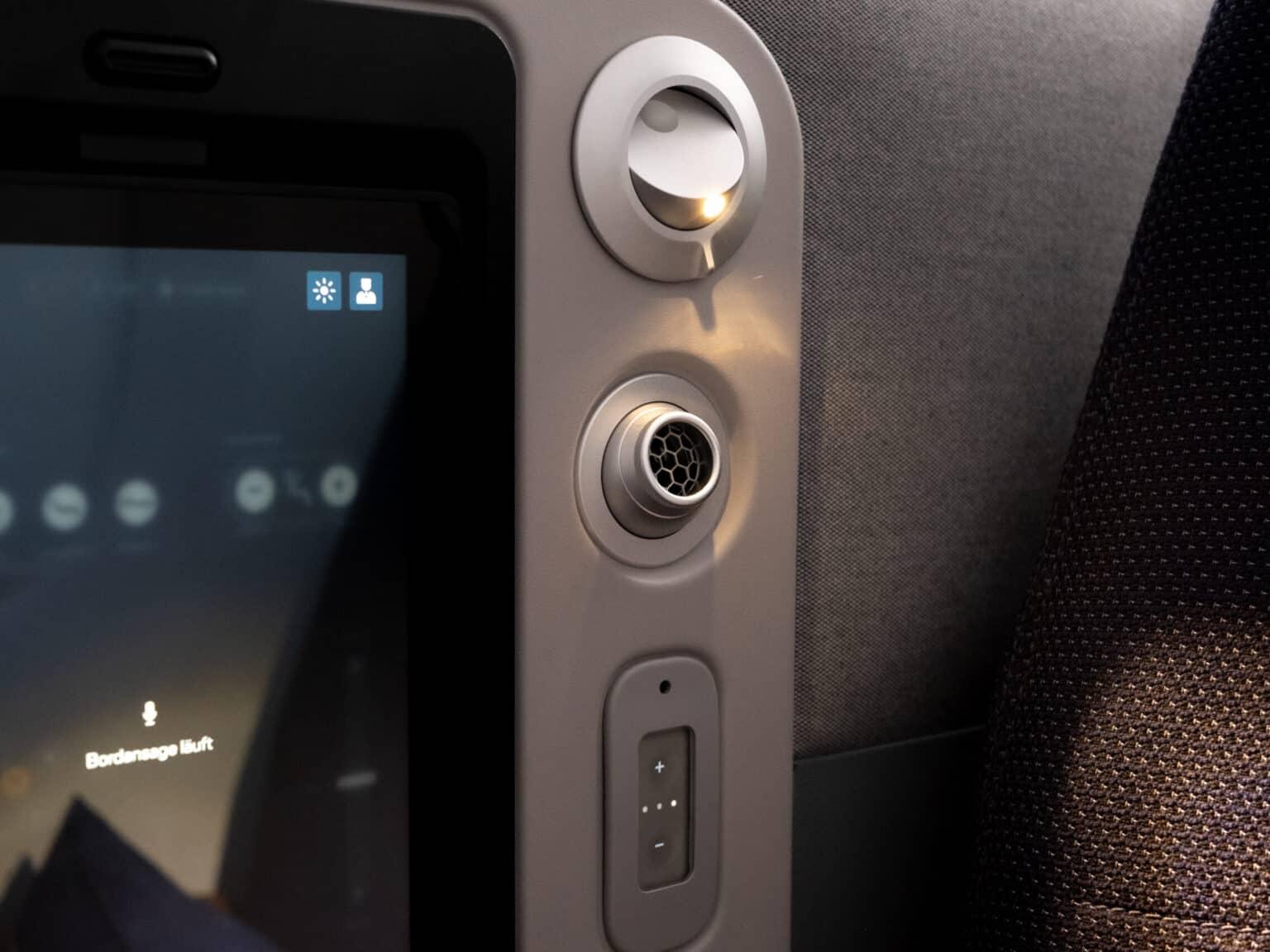A reading lamp next to the screen of an airplane seat.