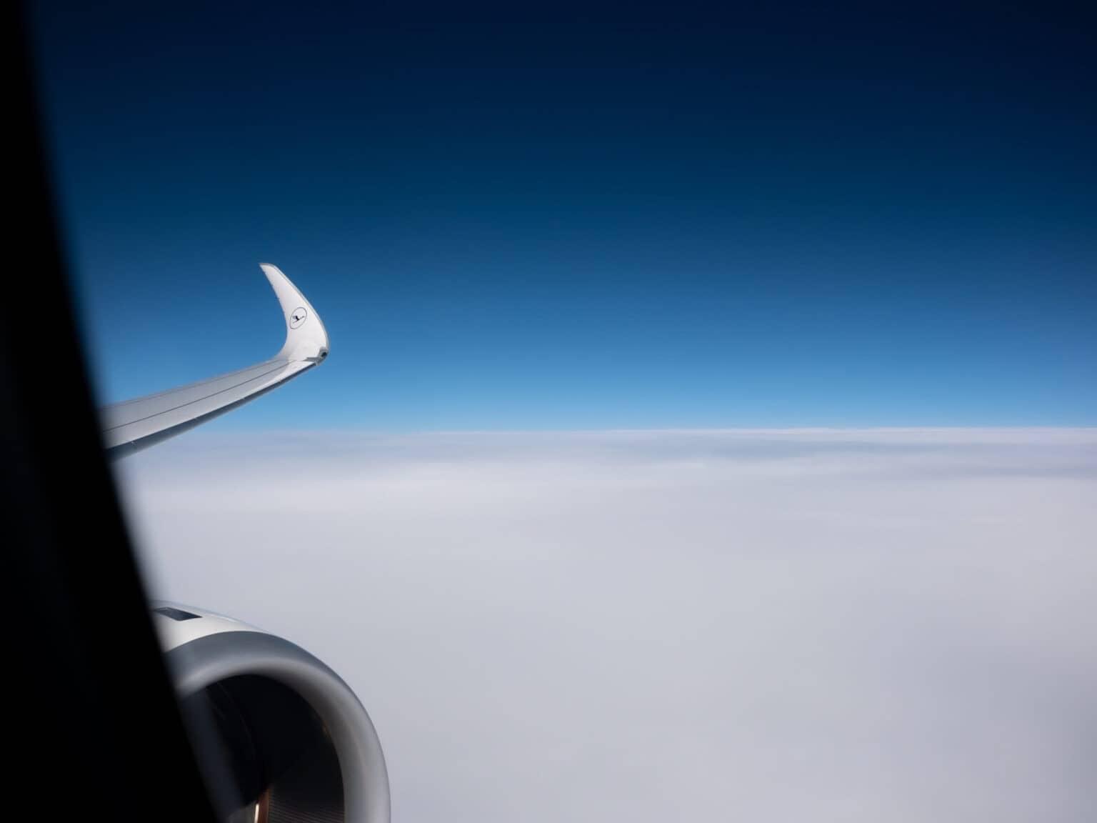 A part of the wing and turbine of an airplane. In the background, a white cloud cover, above it, the blue sky.