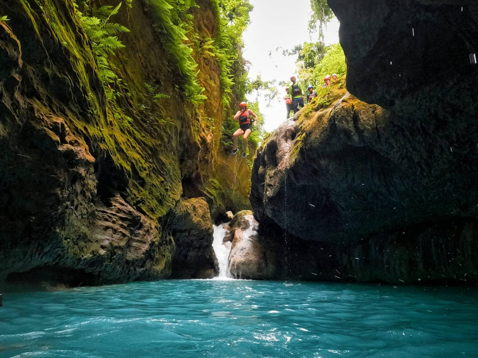Personas con cascos y chalecos salvavidas saltando en el agua turquesa de la garganta.