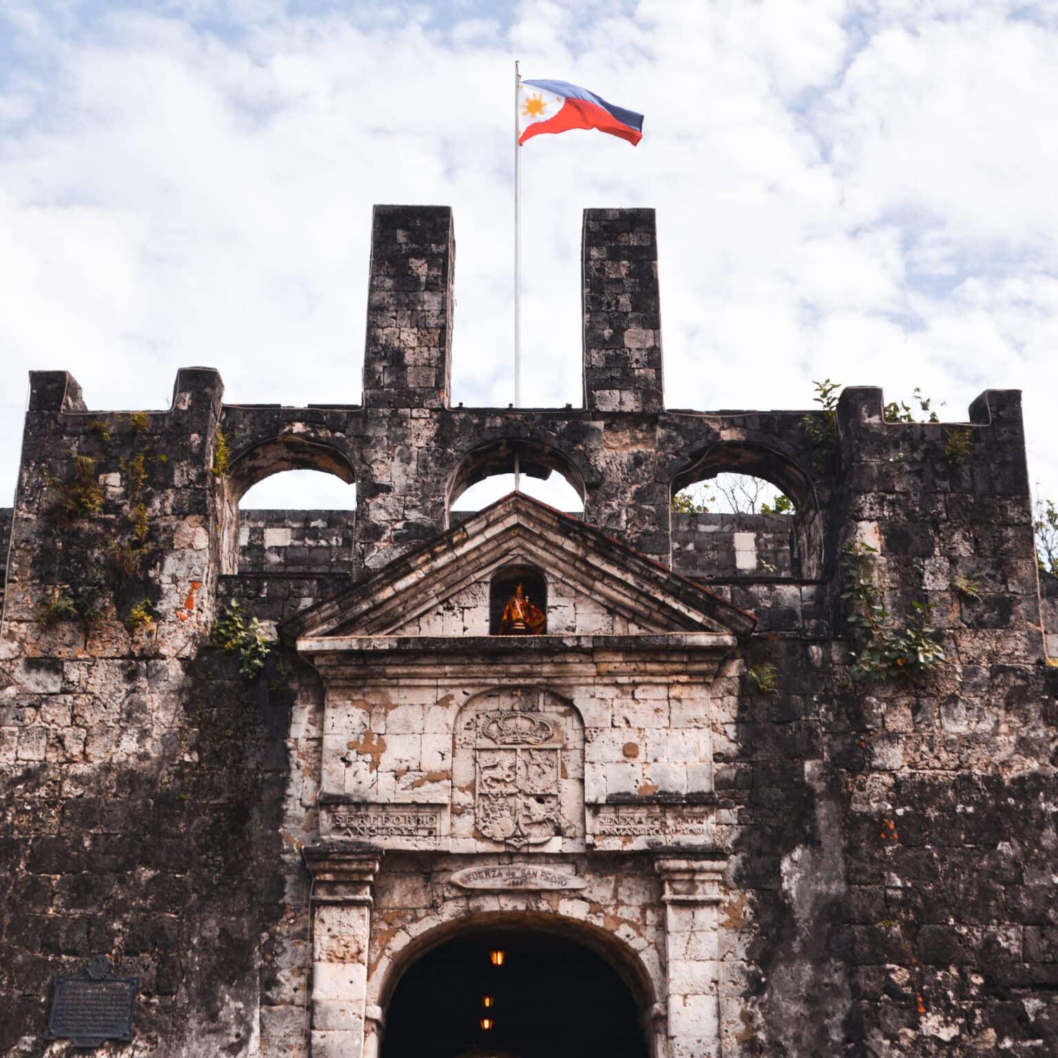 Un antiguo y gran edificio de piedra con la bandera de Filipinas.