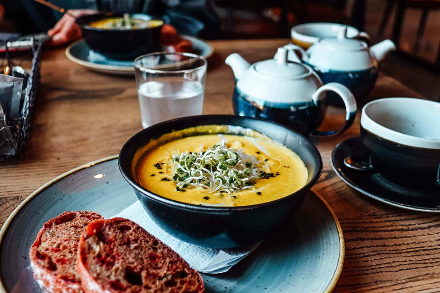 Una sopa amarilla en un tazón, junto a pan en un plato en el Grey Restaurant en Vilnius.
