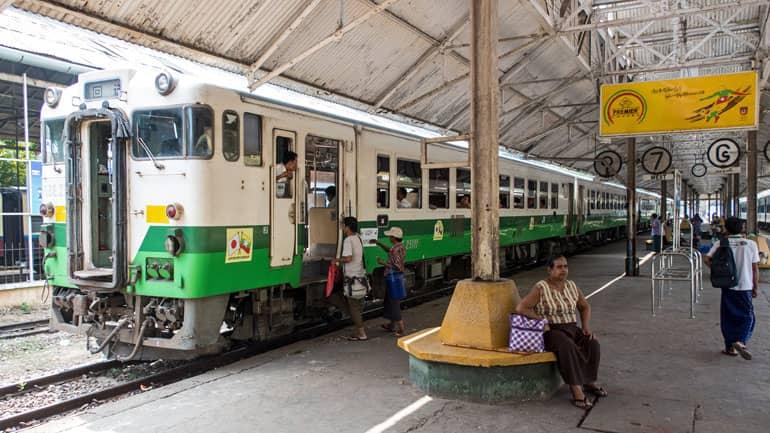 En la estación de tren de Yangón, pasajeros suben a un tren de color verde y blanco.
