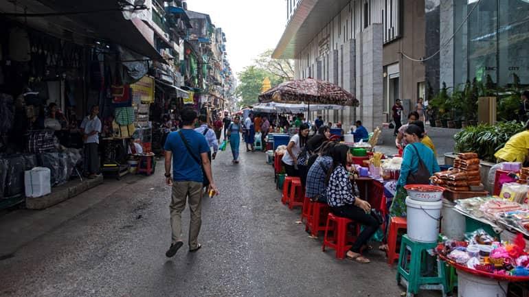 Passersby stroll through the side streets of Yangon, passing food stalls.