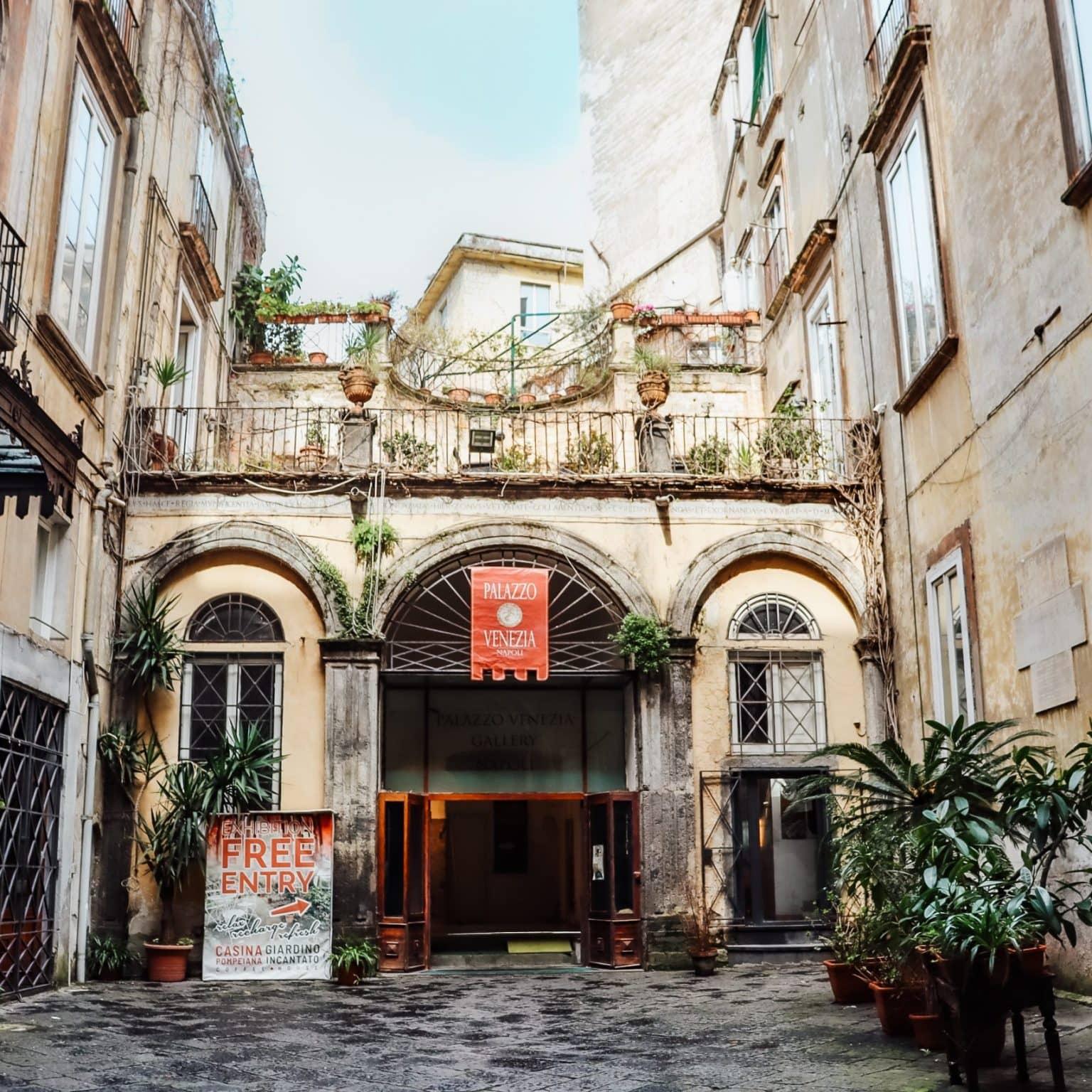 The tall entrance to Palazzo Venezia is decorated with plants, with the sky and courtyards of surrounding buildings visible in the background.