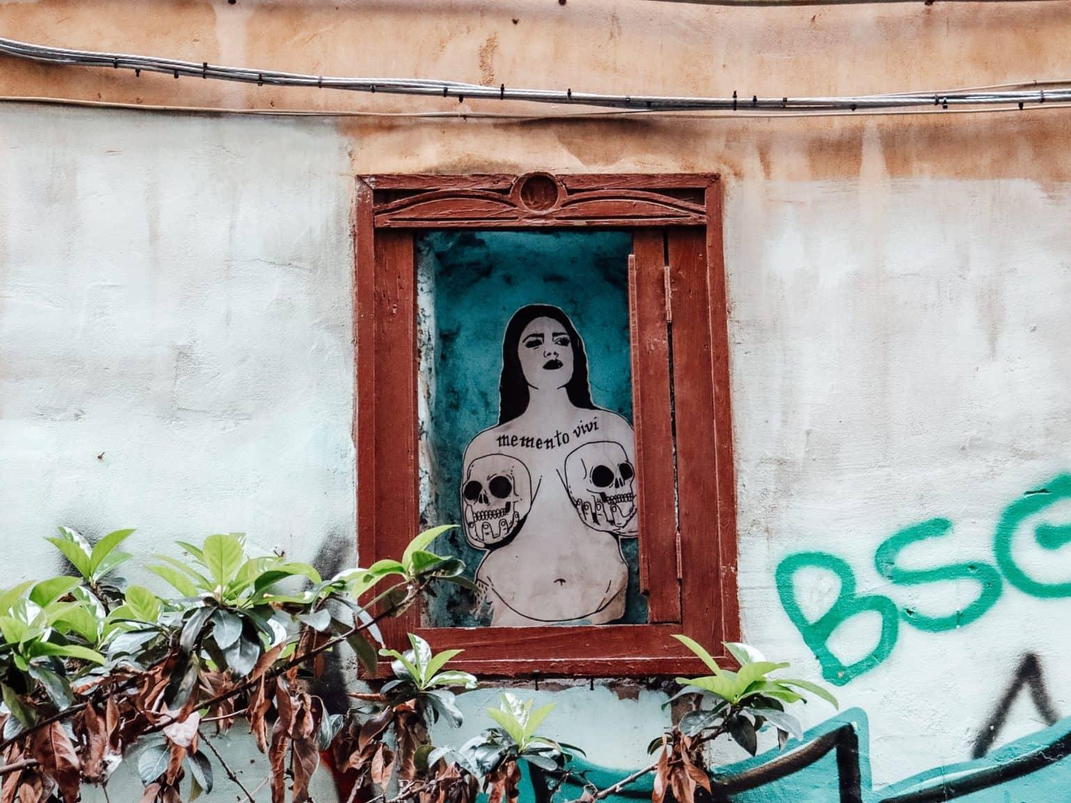 The image of a woman holding skulls has been painted directly onto the wooden slats of a wall.