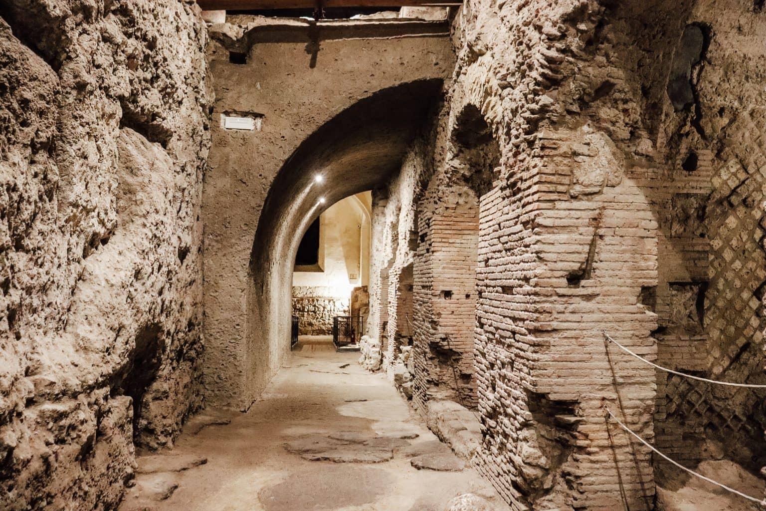 An underground passage in San Lorenzo Maggiore with semi-circular arches and ancient rock remnants.