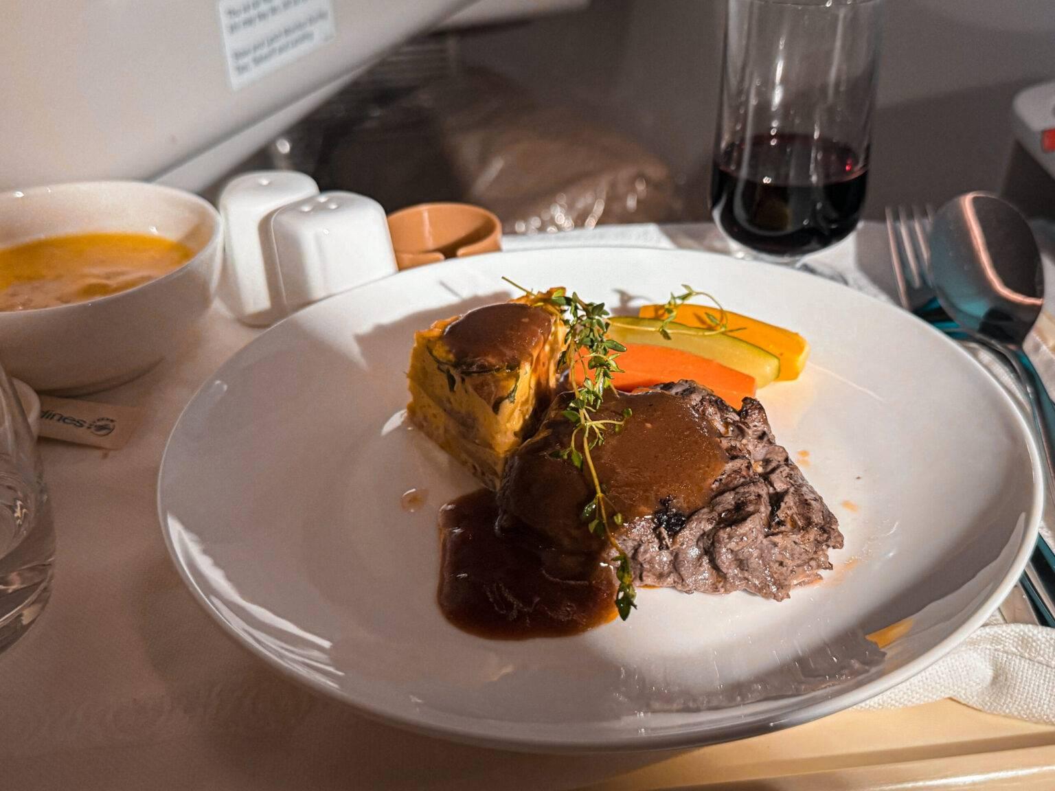 A steak and vegetables on a plate in the airplane from Vietnam Airlines.