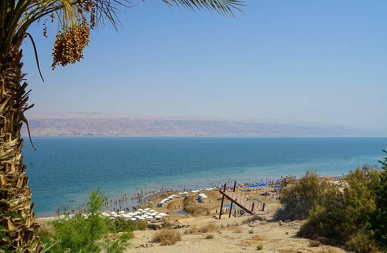 En la orilla arenosa del Mar Muerto, Kalia Beach en Israel, los bañistas se agrupan bajo sombrillas blancas y en la orilla del agua.