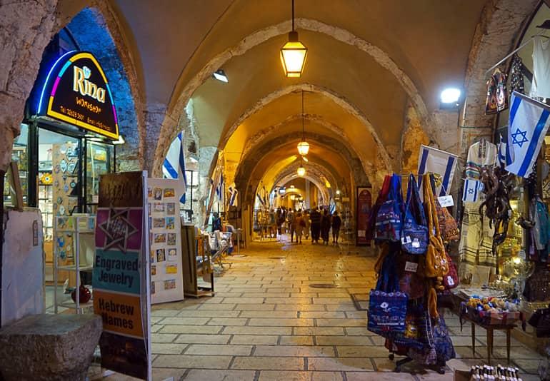 Bajo arcos iluminados en la Ciudad Vieja de Jerusalén, los comerciantes ofrecen sus productos en pequeñas tiendas.