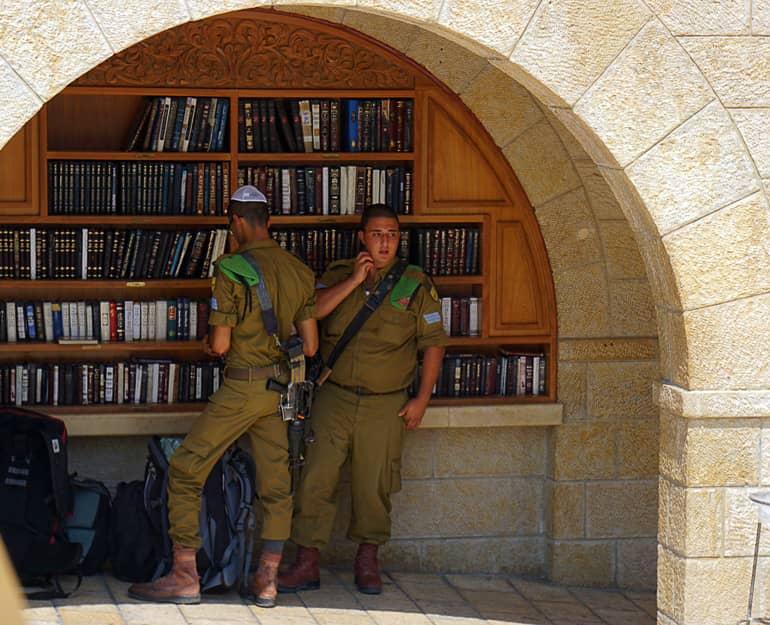 Dos soldados israelíes armados están en uniforme verde bajo un arco en una estantería de libros en Jerusalén.