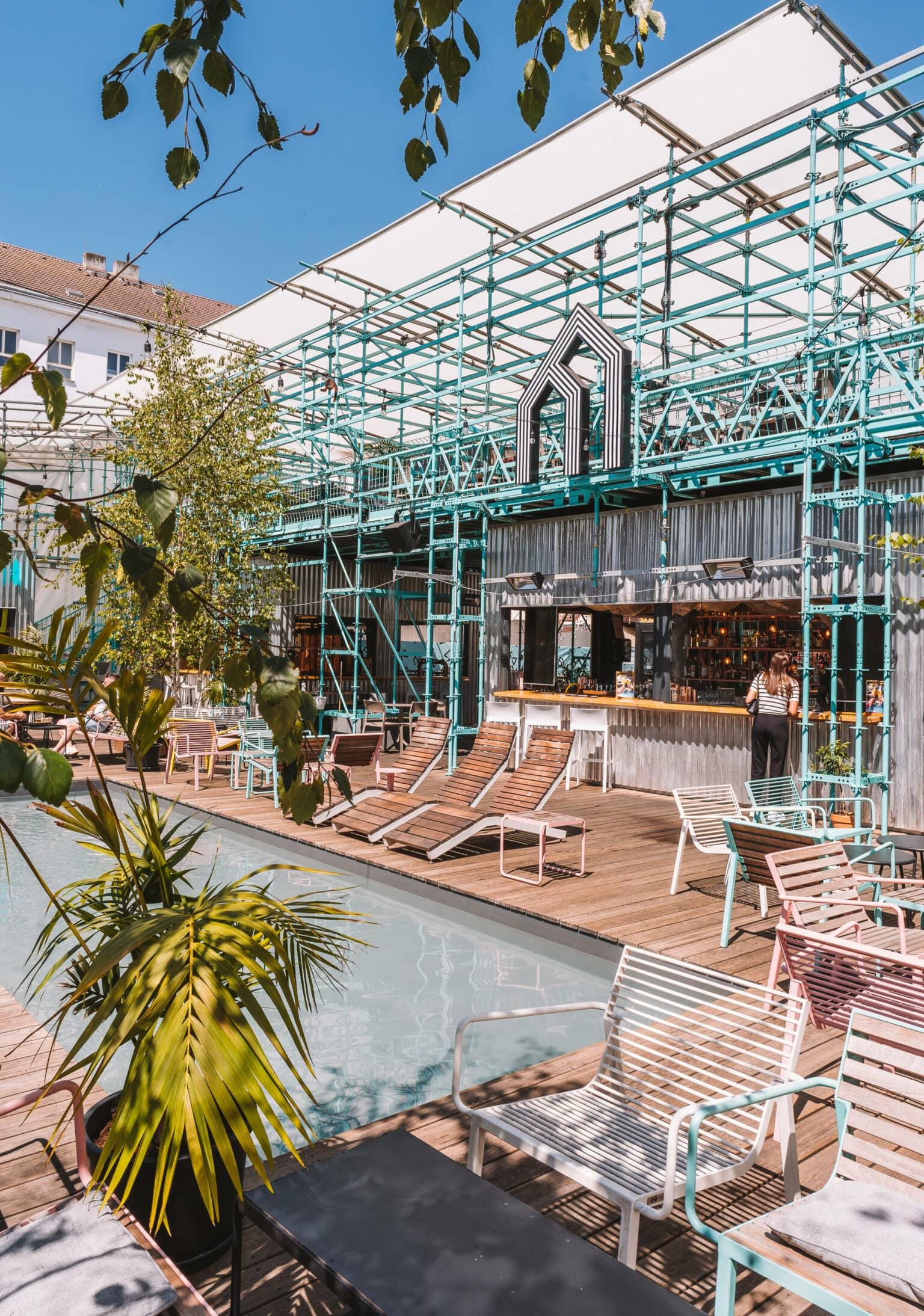 The exterior of the Manifesto Anděl Food Market with colorful chairs and a small pool in Prague.