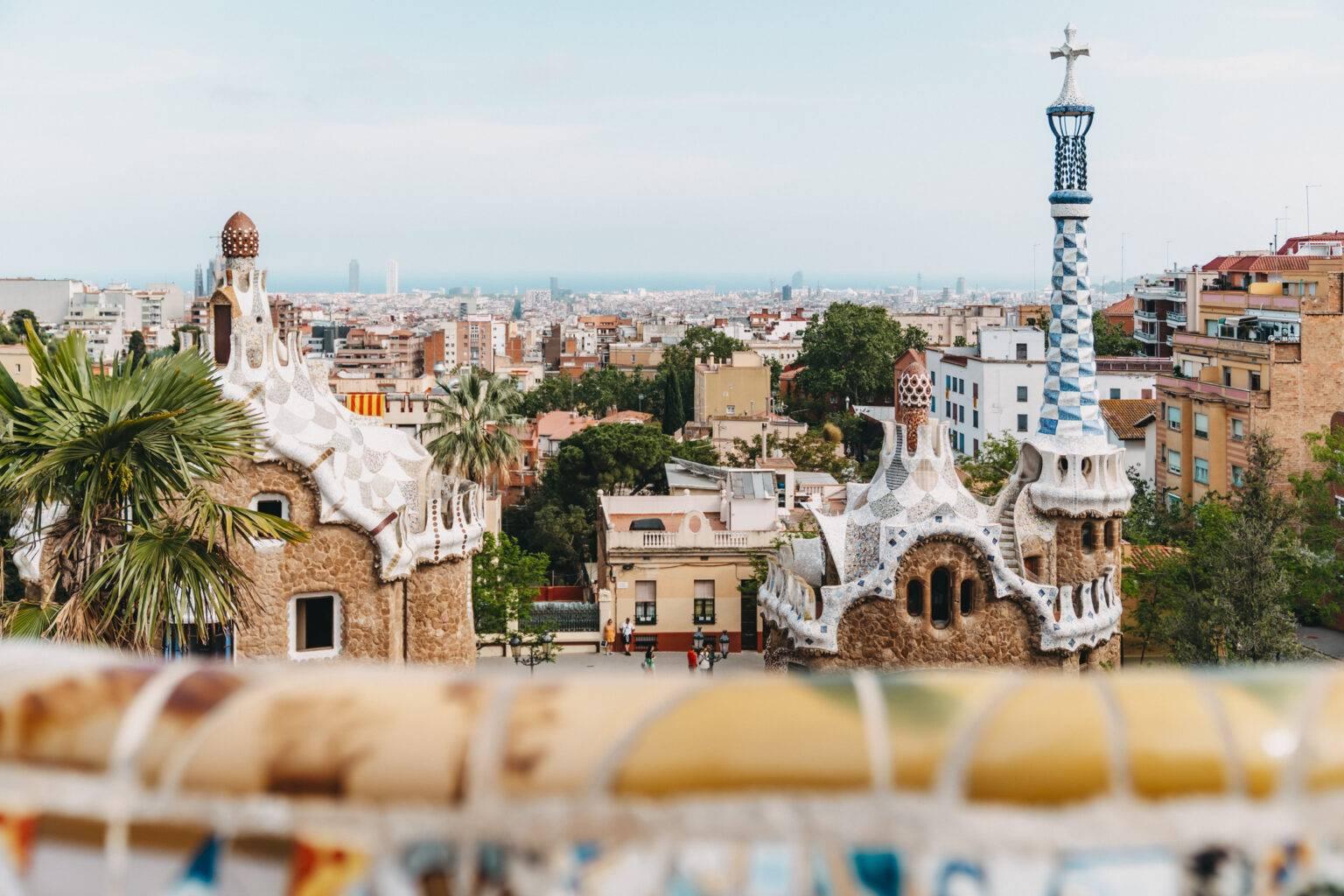 The skyline of Barcelona from the perspective of Park Güell. In the foreground are the mosaic-adorned buildings at the park entrance, and in the background is the sea.