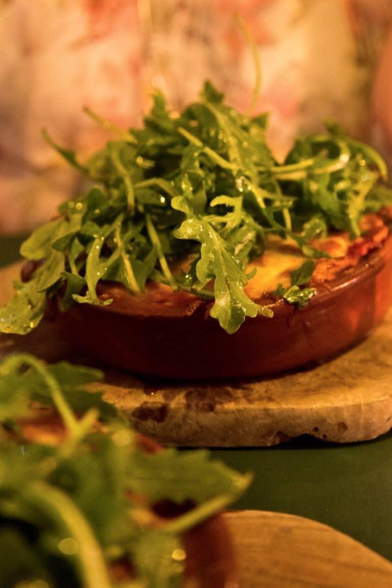 En una tabla de madera se sirve un molde de lasaña con rucola fresca en el café Taxa de Copenhague.