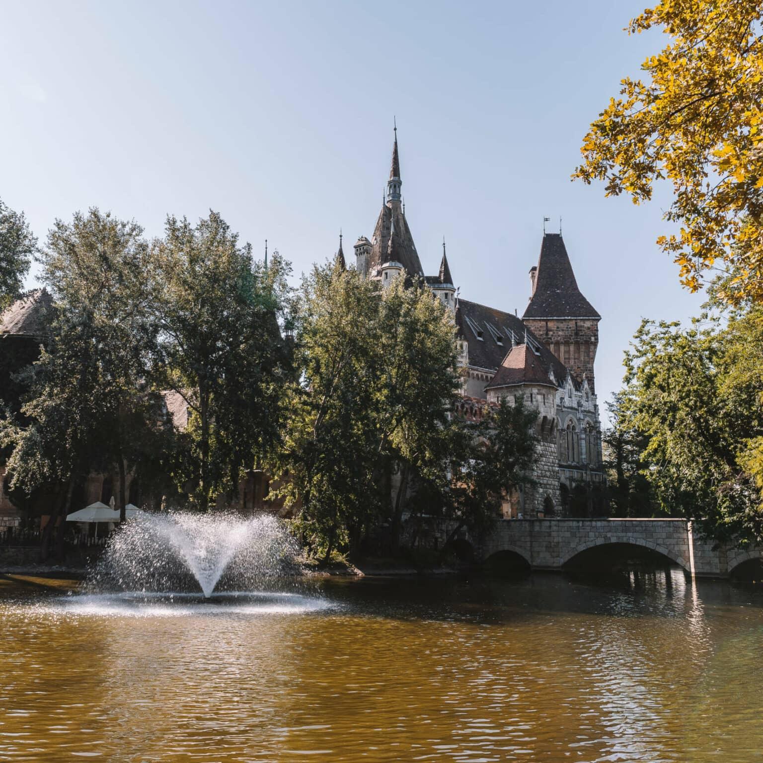 El antiguo castillo Vajdahunyad en Budapest asomándose detrás de un lago y árboles.