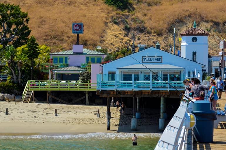 At the Santa Monica Pier in Los Angeles, visitors watch the activities by the water, with the Malibu Farm restaurant visible in the background.