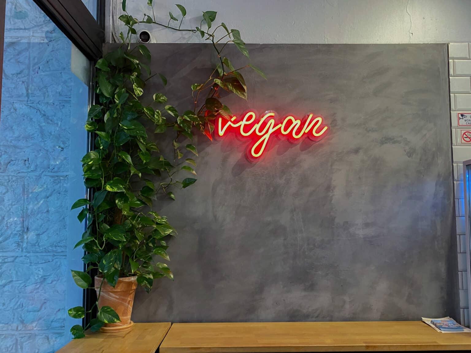 Neon sign reading "vegan" on a gray wall.