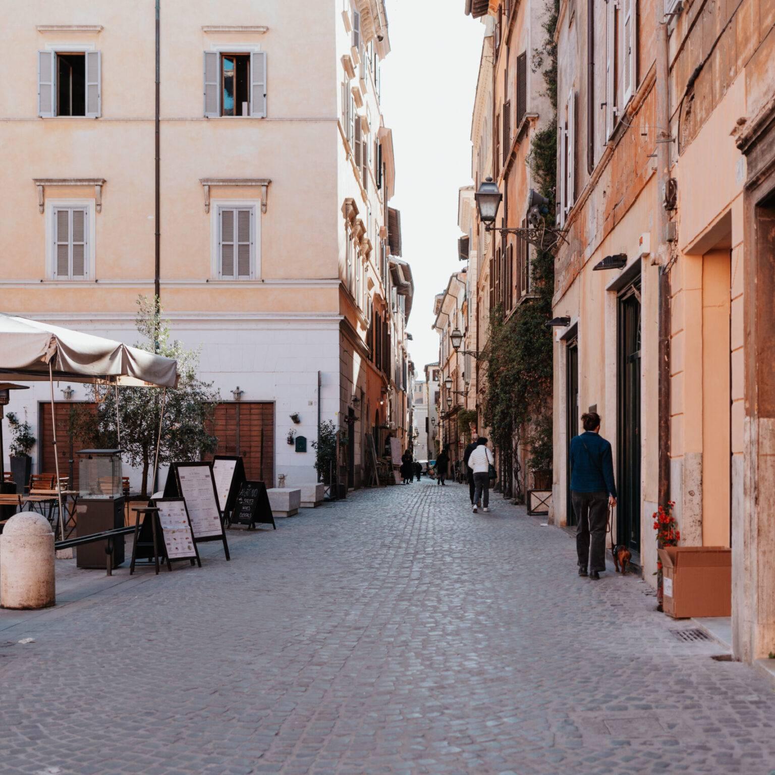 Via Coronari in Rome with cobblestones, cafés, historic facades, and passersby.