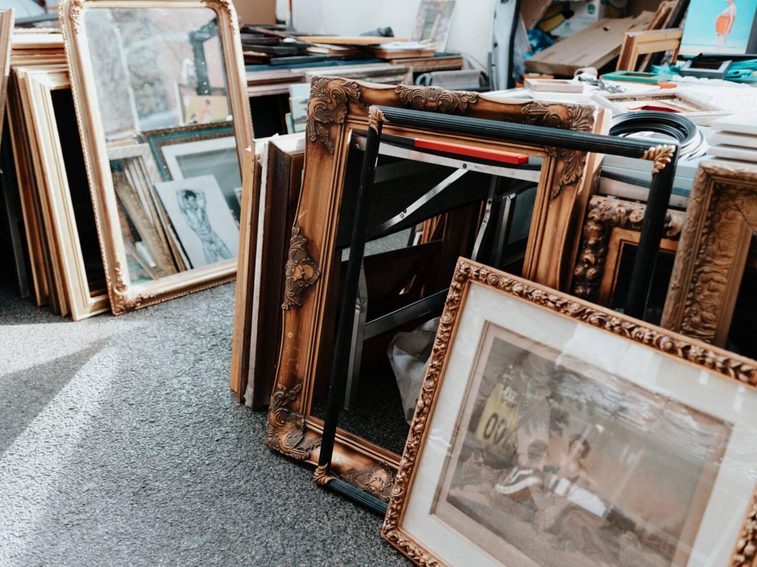 A market stall with rows of antique picture frames and artworks.