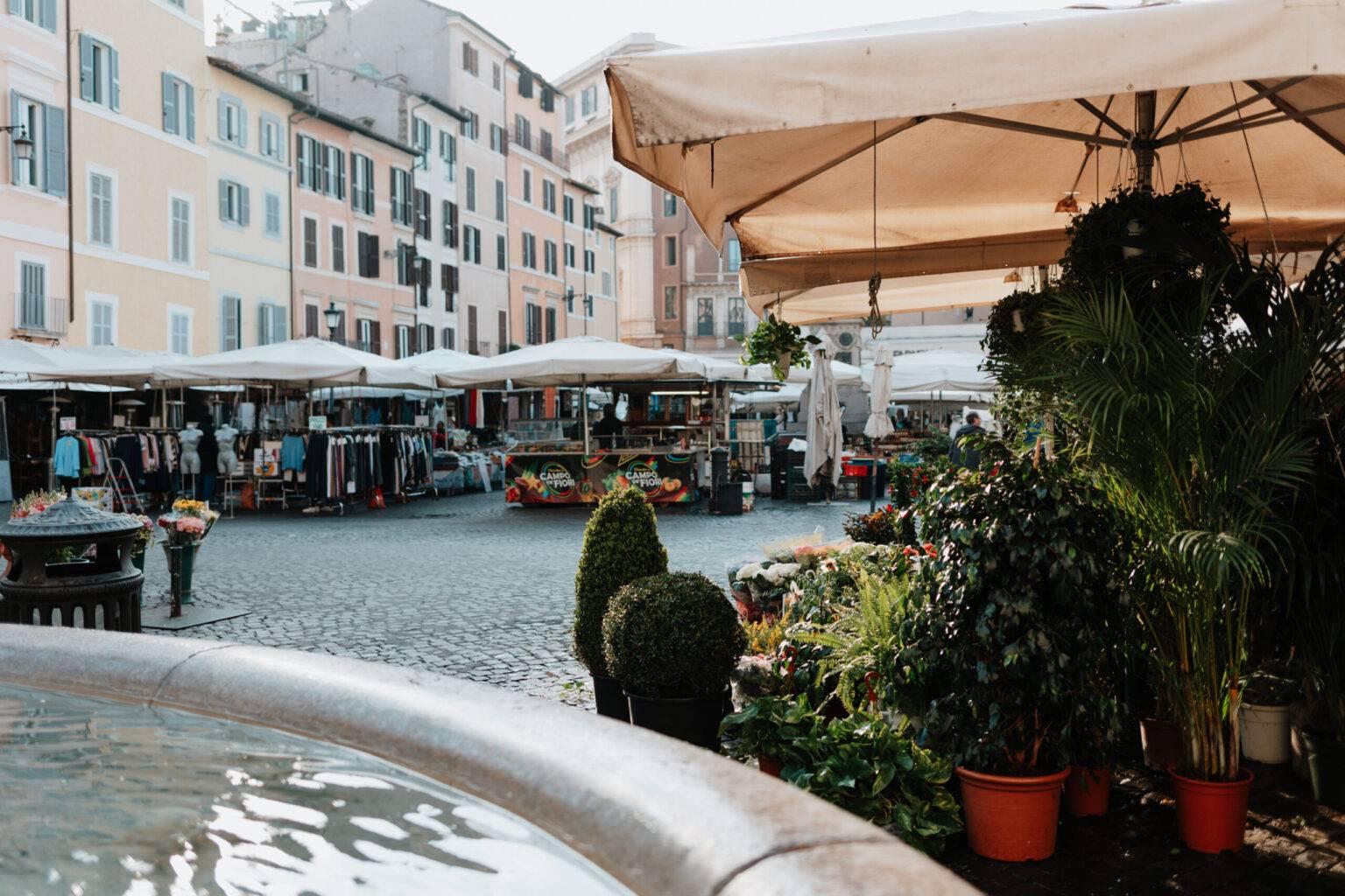 Colorful weekly market at Campo de' Fiori in Rome with flowers and vegetable stalls.