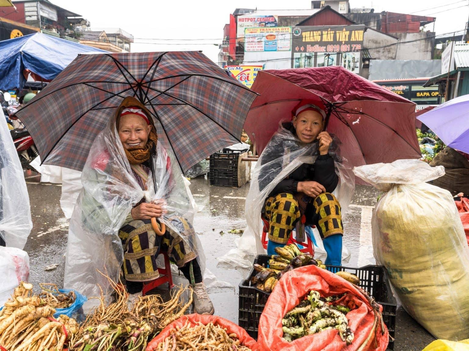 Two vendors at the Sa Pa market protect themselves from the rain with umbrellas.