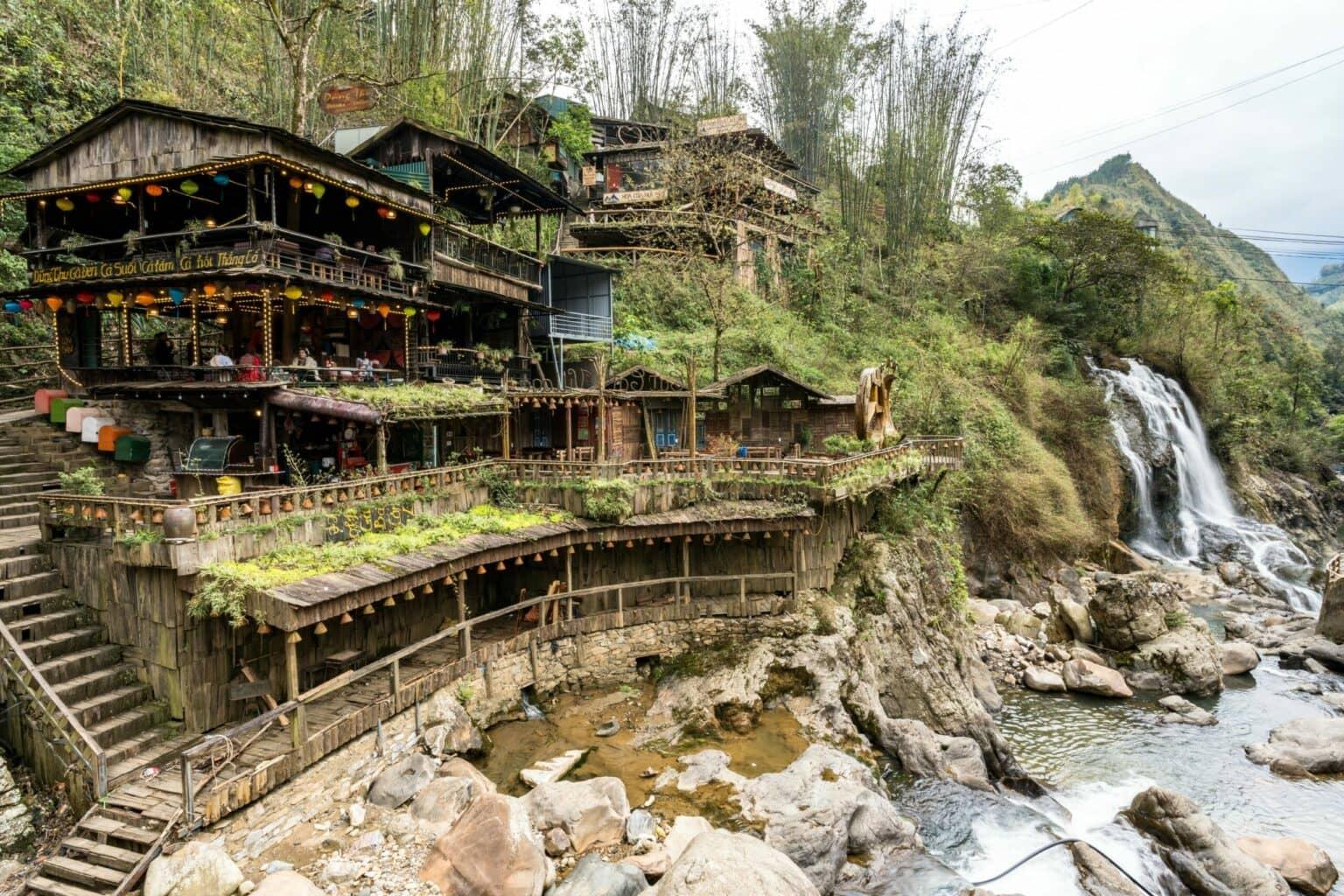 A house by a river with a waterfall in Cat Cat Village.