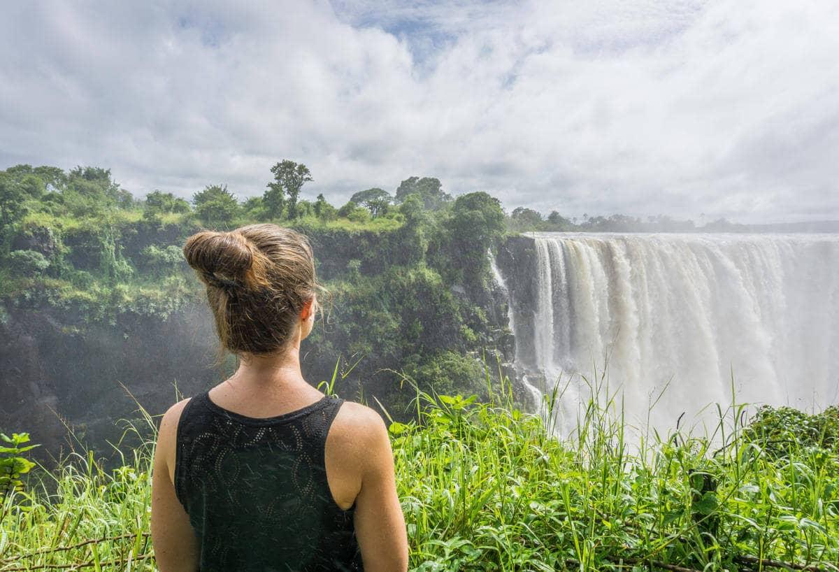 Una mujer con una camiseta negra y un moño dirige su mirada hacia las Cataratas Victoria de Zimbabue.