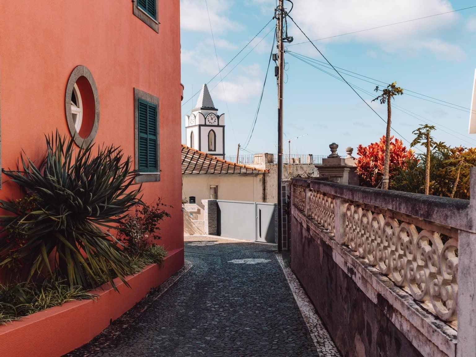A narrow alley leads past an orange house with a view of the horizon